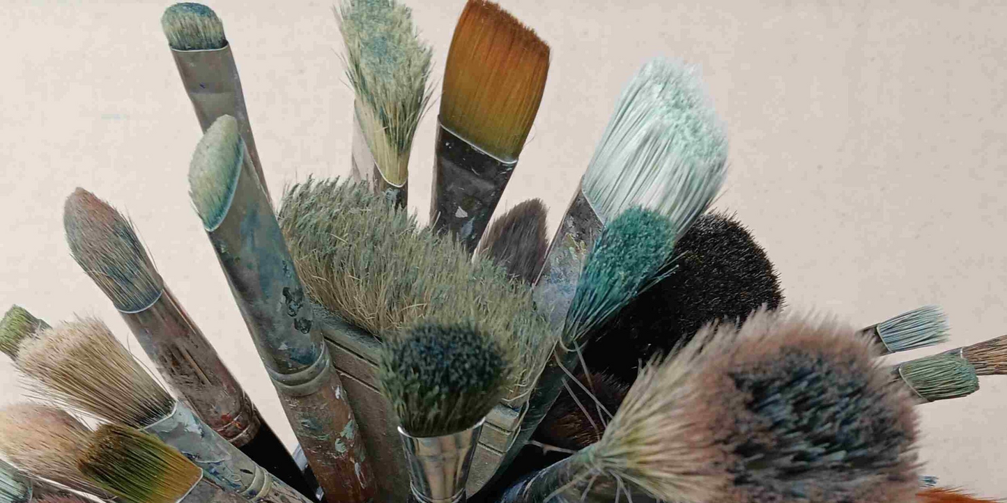 Collection of artists paintbrushes with bristles showing wear on a textured background