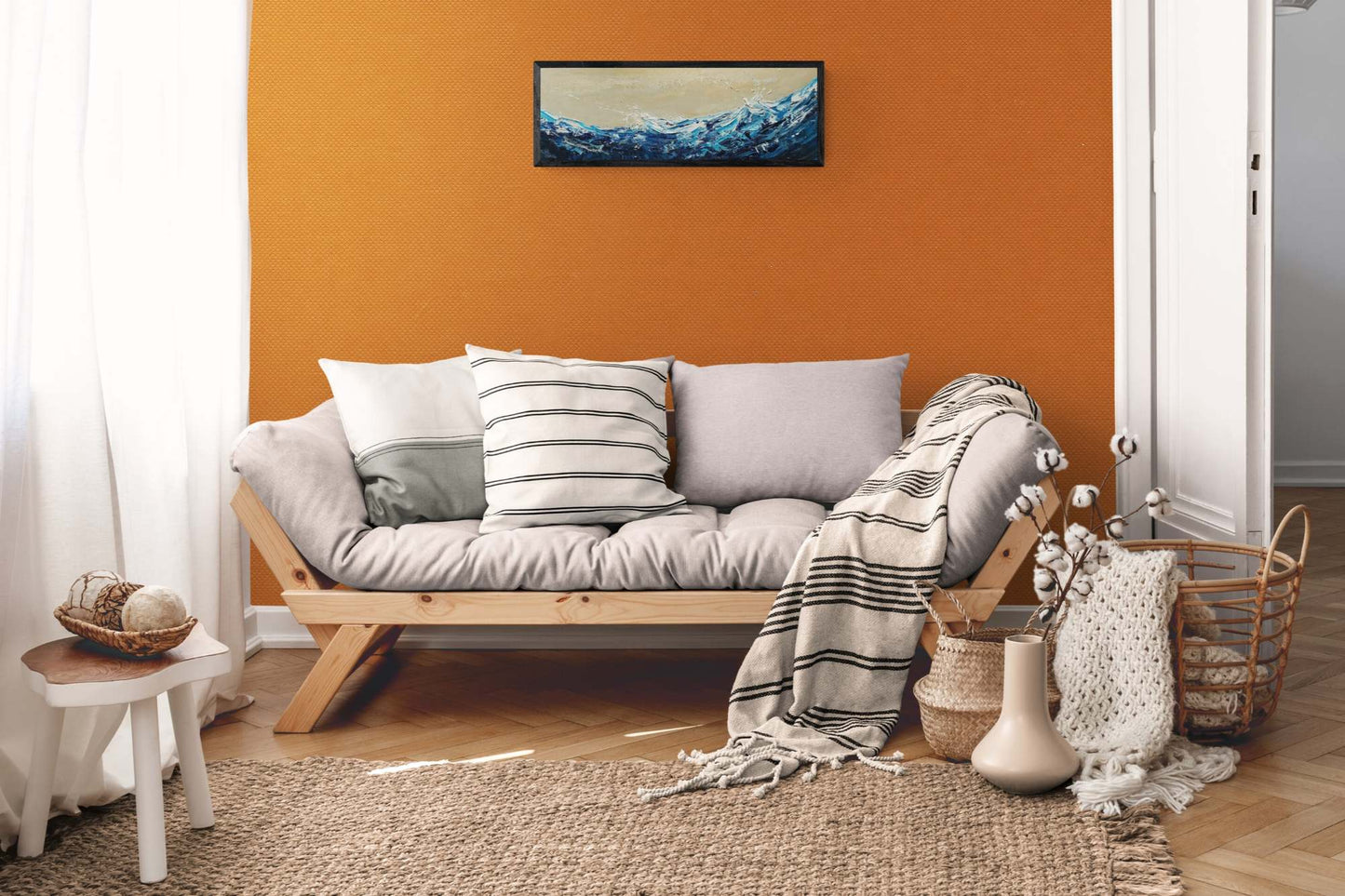Cozy living room with a gray sofa, striped cushions, and a blanket against an orange wall with a seascape oil painting.